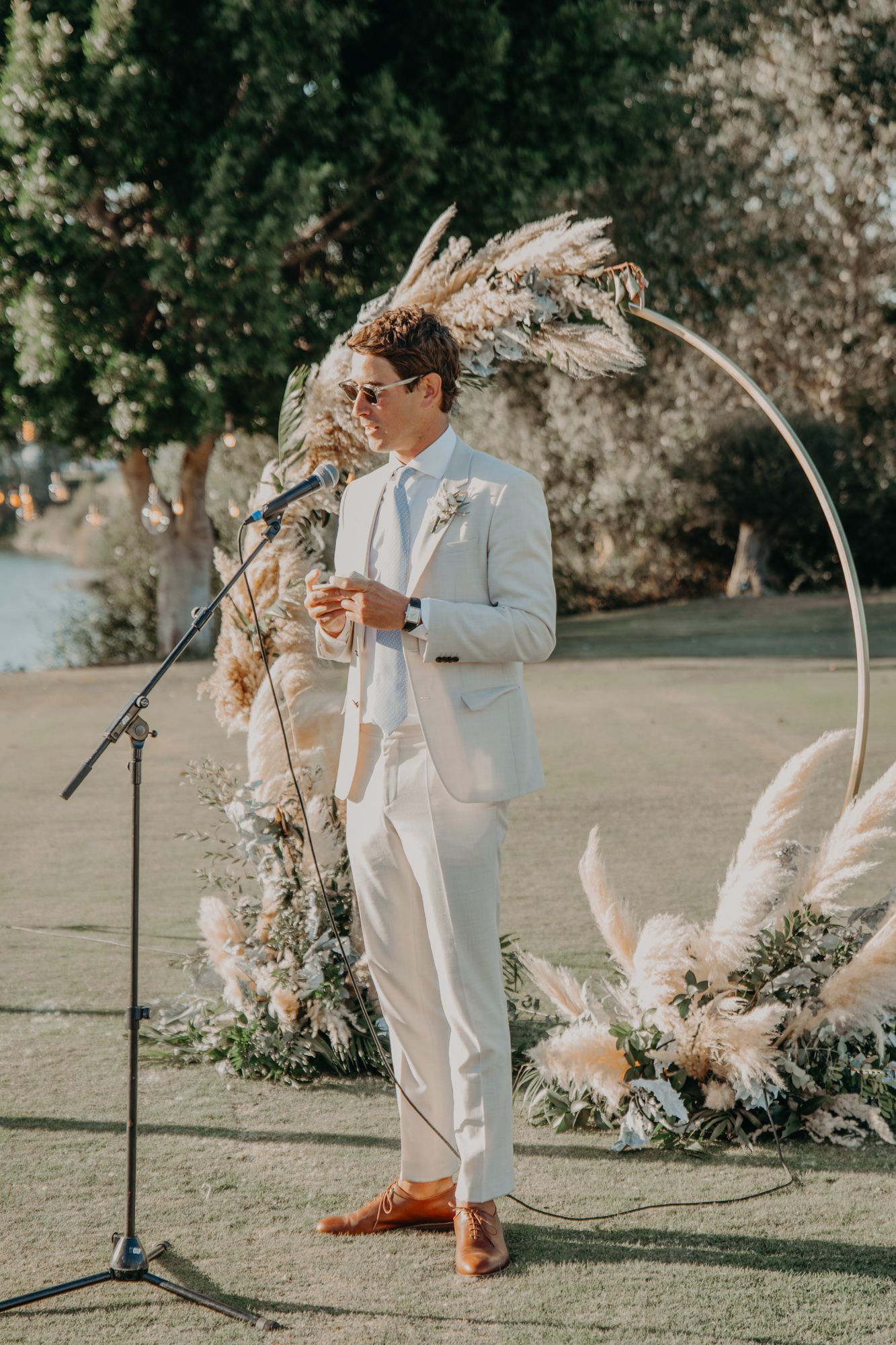 Speaker delivers speech at outdoor ceremony with pampas grass arch decoration.