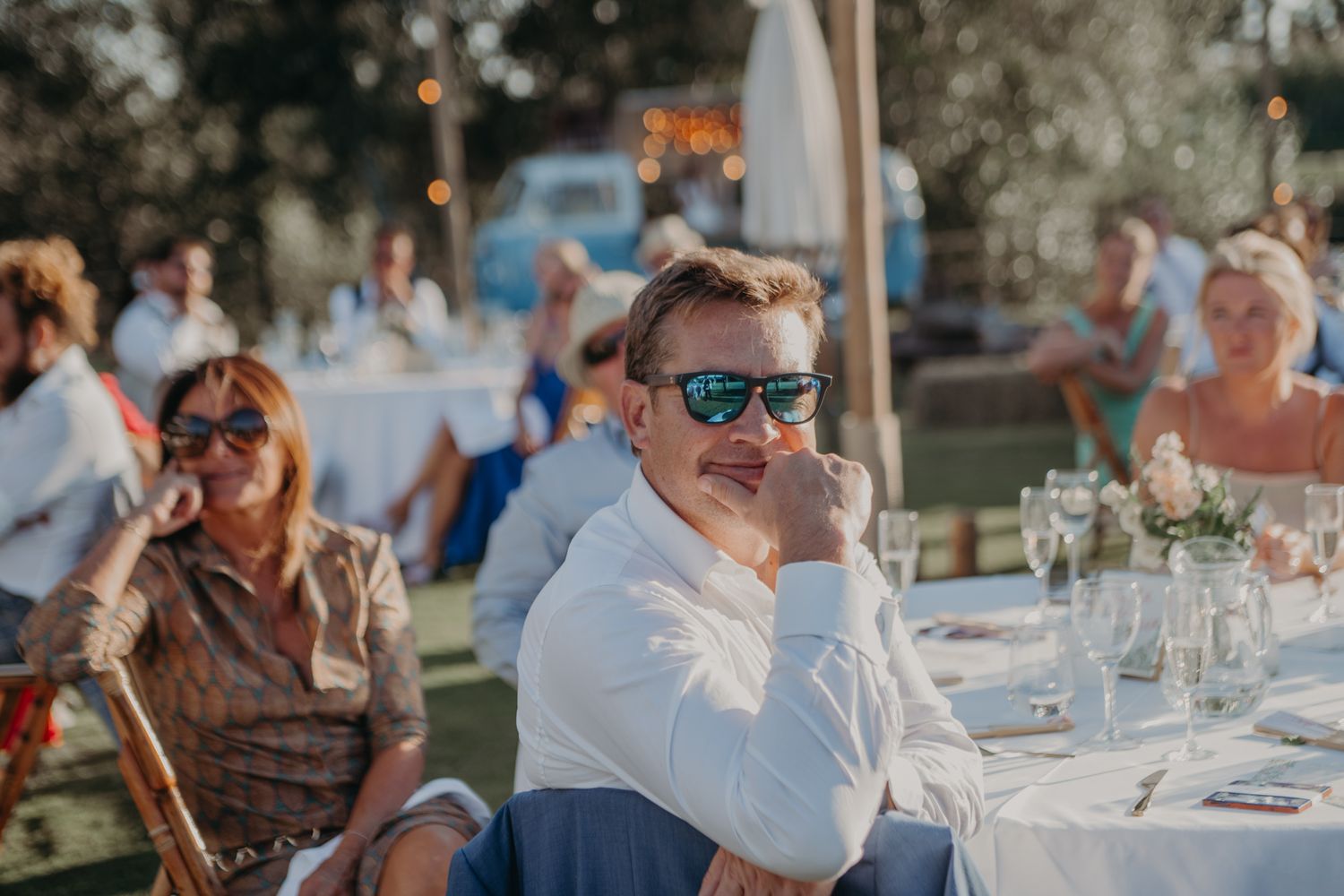 Wedding guest enjoying an outdoor reception wearing sunglasses and white shirt.