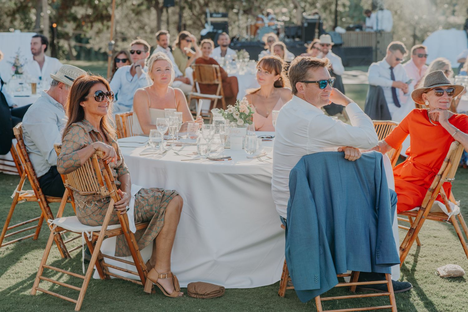 Wedding guests enjoying an outdoor reception at round tables under sunny skies.