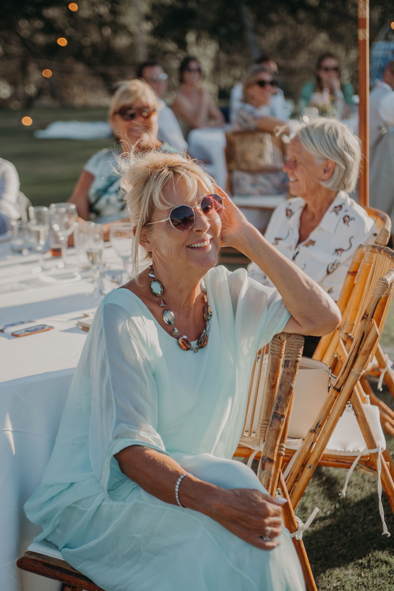 A guest in sunglasses and turquoise dress enjoys an outdoor wedding reception on a sunny afternoon.