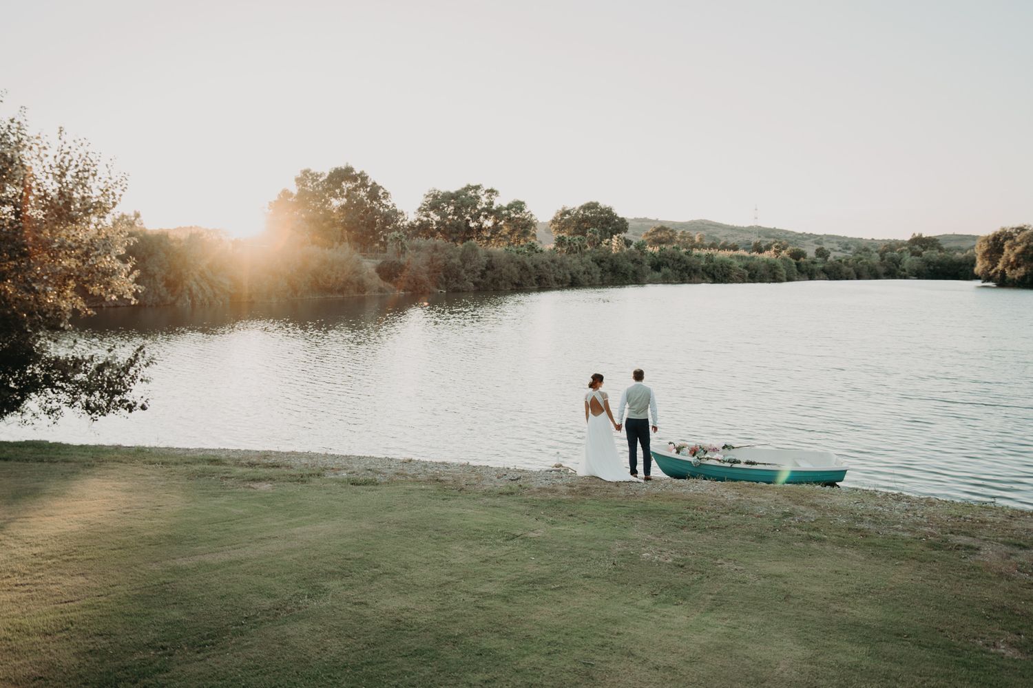 Sunset view of a couple standing by a lake with a small boat nearby.