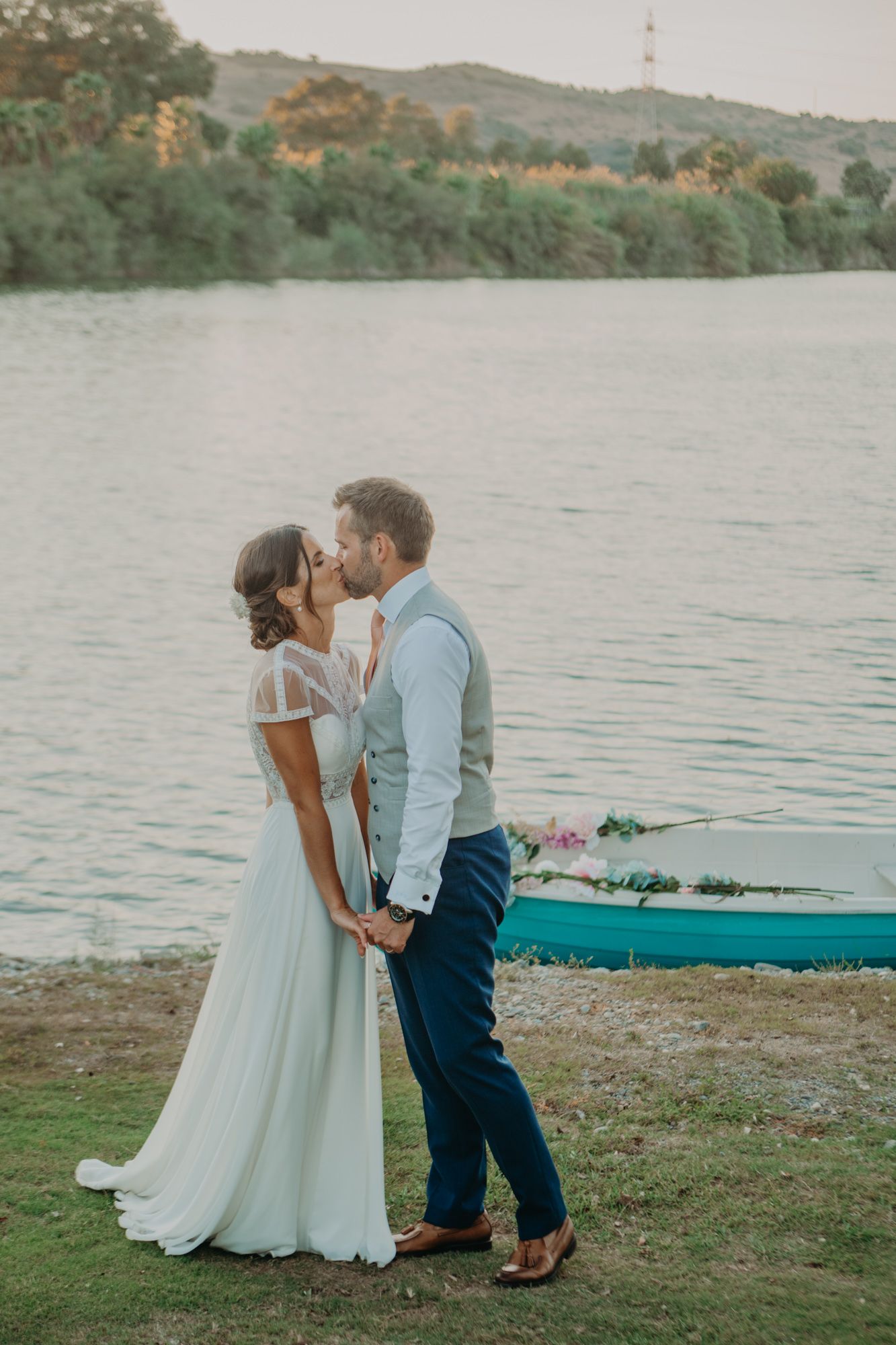 Couple sharing a romantic kiss by a lake at sunset with a kayak in the background.
