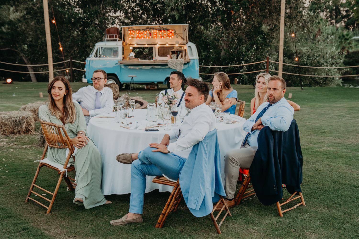 Wedding guests seated at an outdoor dinner table with string lights overhead.
