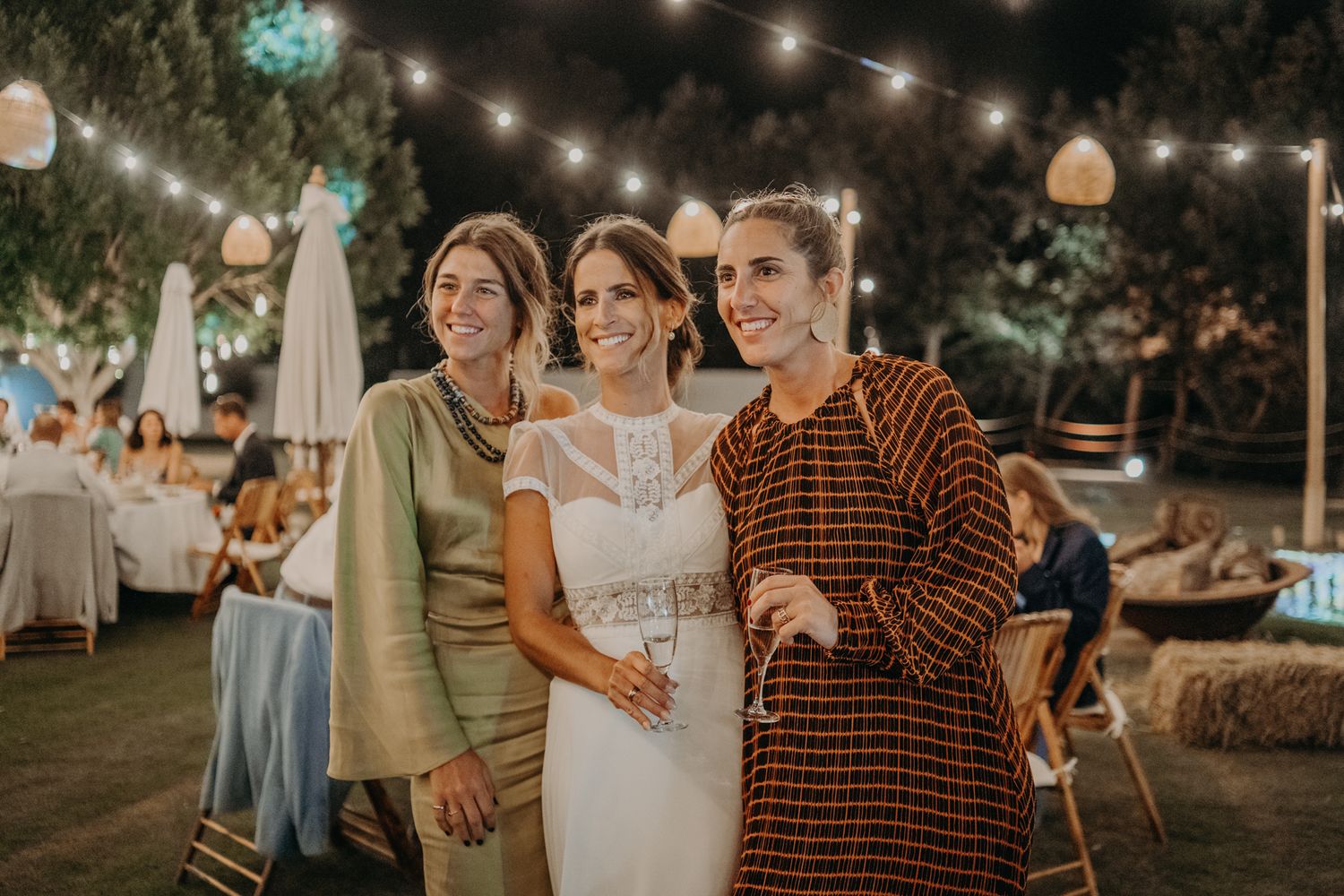 An outdoor wedding reception with string lights and guests celebrating in a garden setting at dusk.