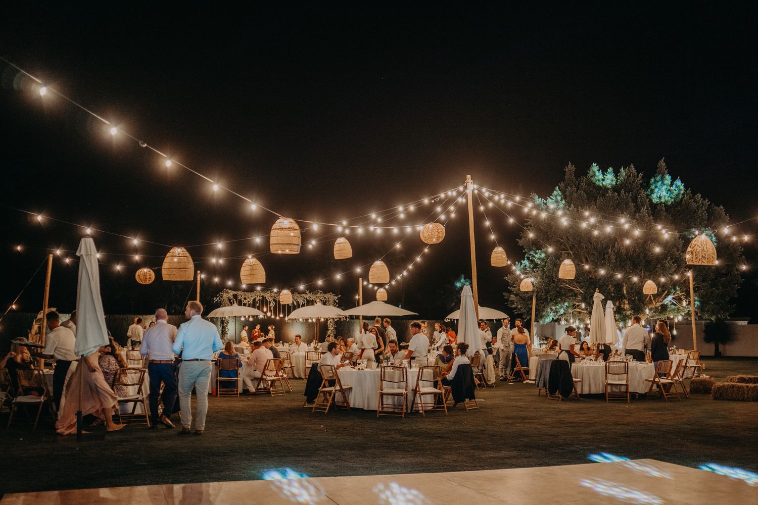 An evening outdoor wedding reception with string lights illuminating tables and guests under the night sky.