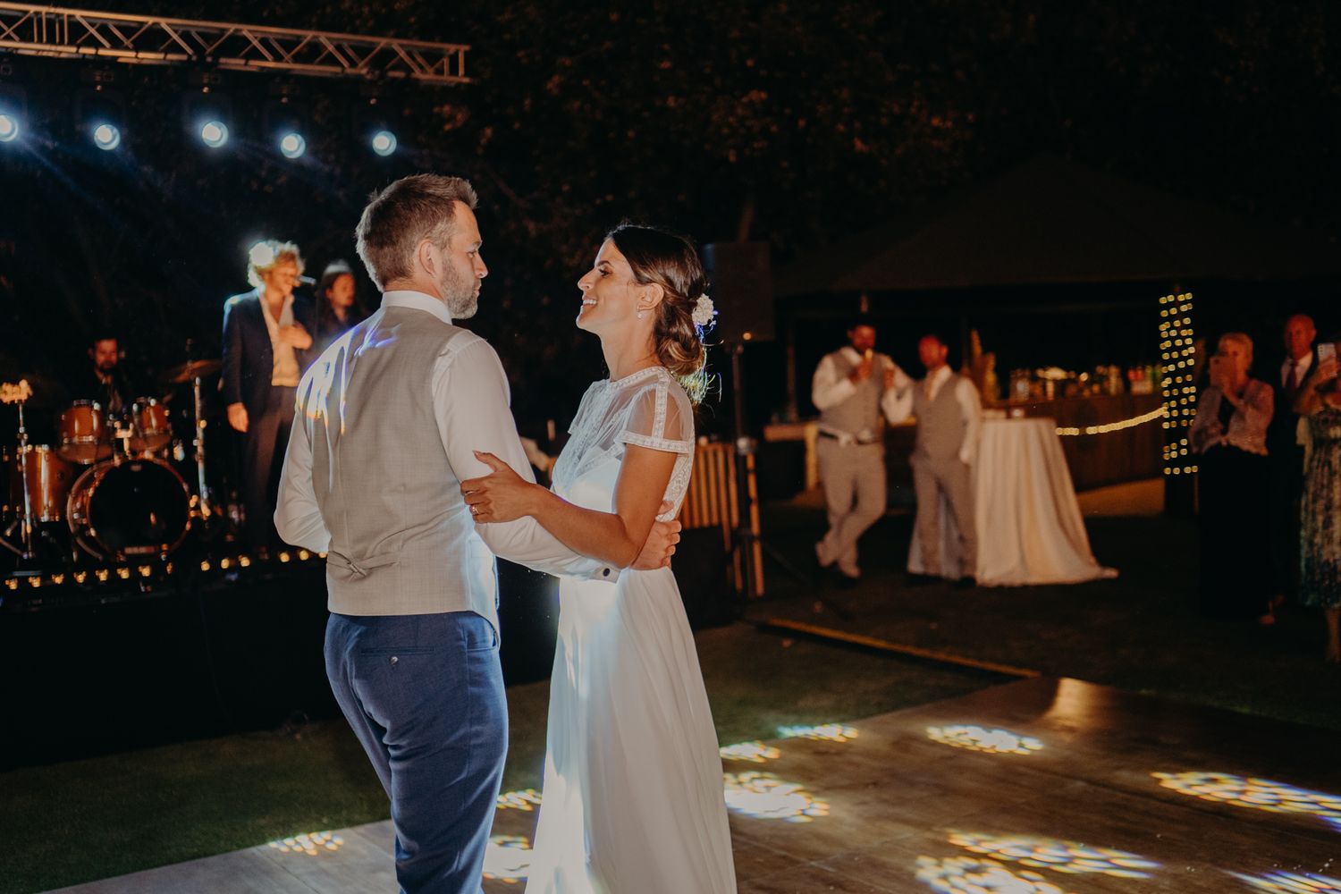 A couple sharing their first dance at an outdoor evening wedding reception with string lights overhead.