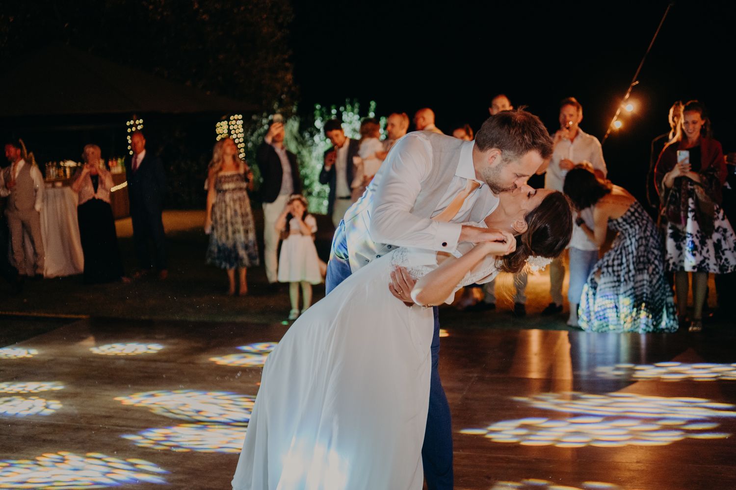 Wedding guests dancing on an illuminated dance floor during an evening reception.