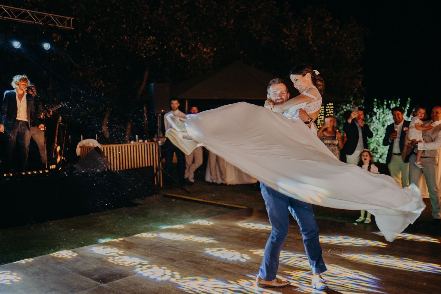 A couple dances at their wedding reception as the groom lifts the bride's flowing white dress in a dramatic twirl.