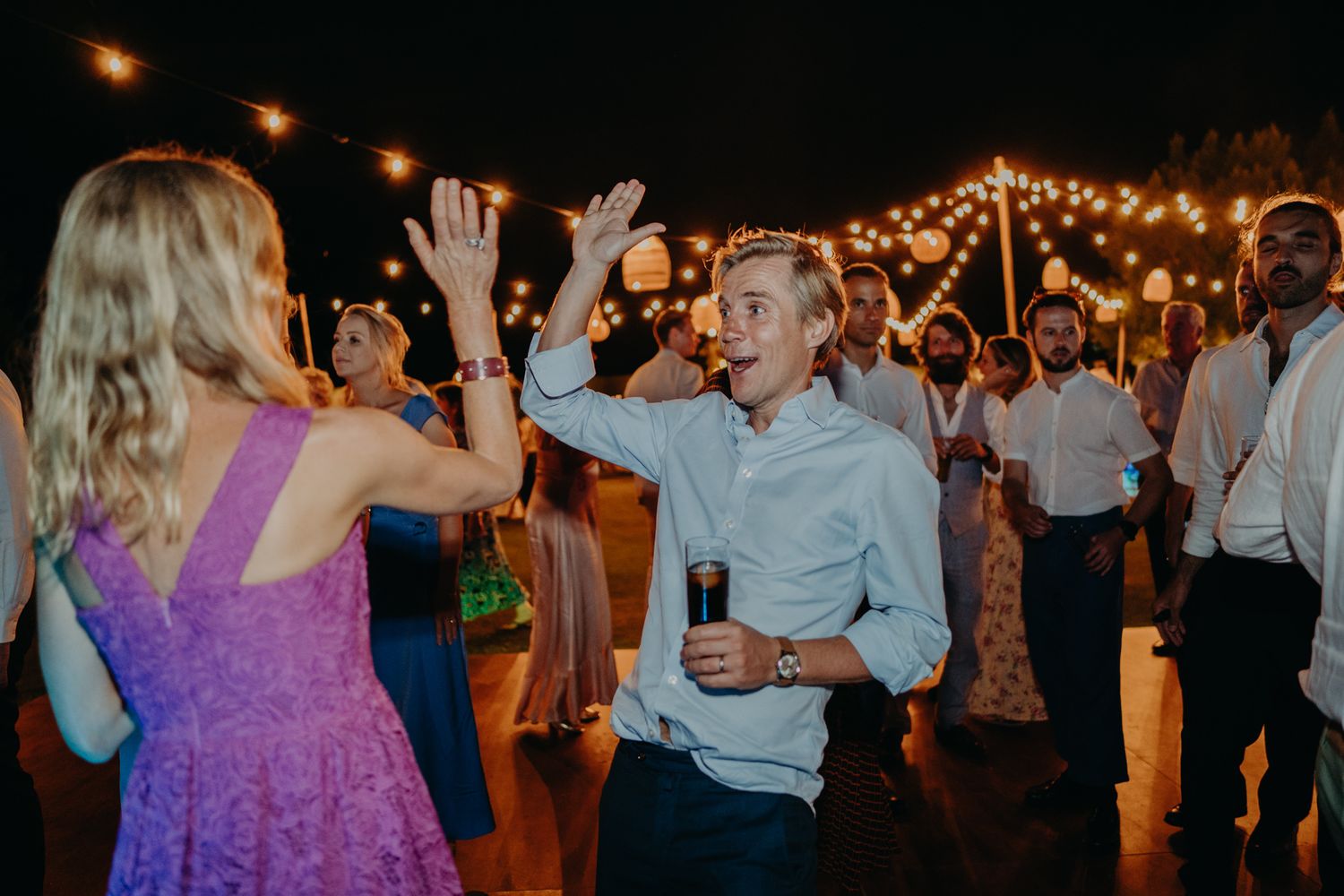 Wedding guests dancing and celebrating on the dance floor under string lights.