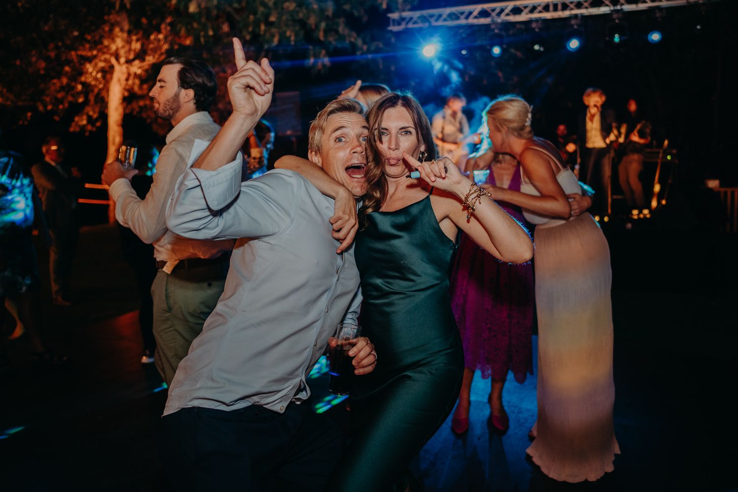 Guests dancing and celebrating energetically at a nighttime wedding reception with stage lighting.