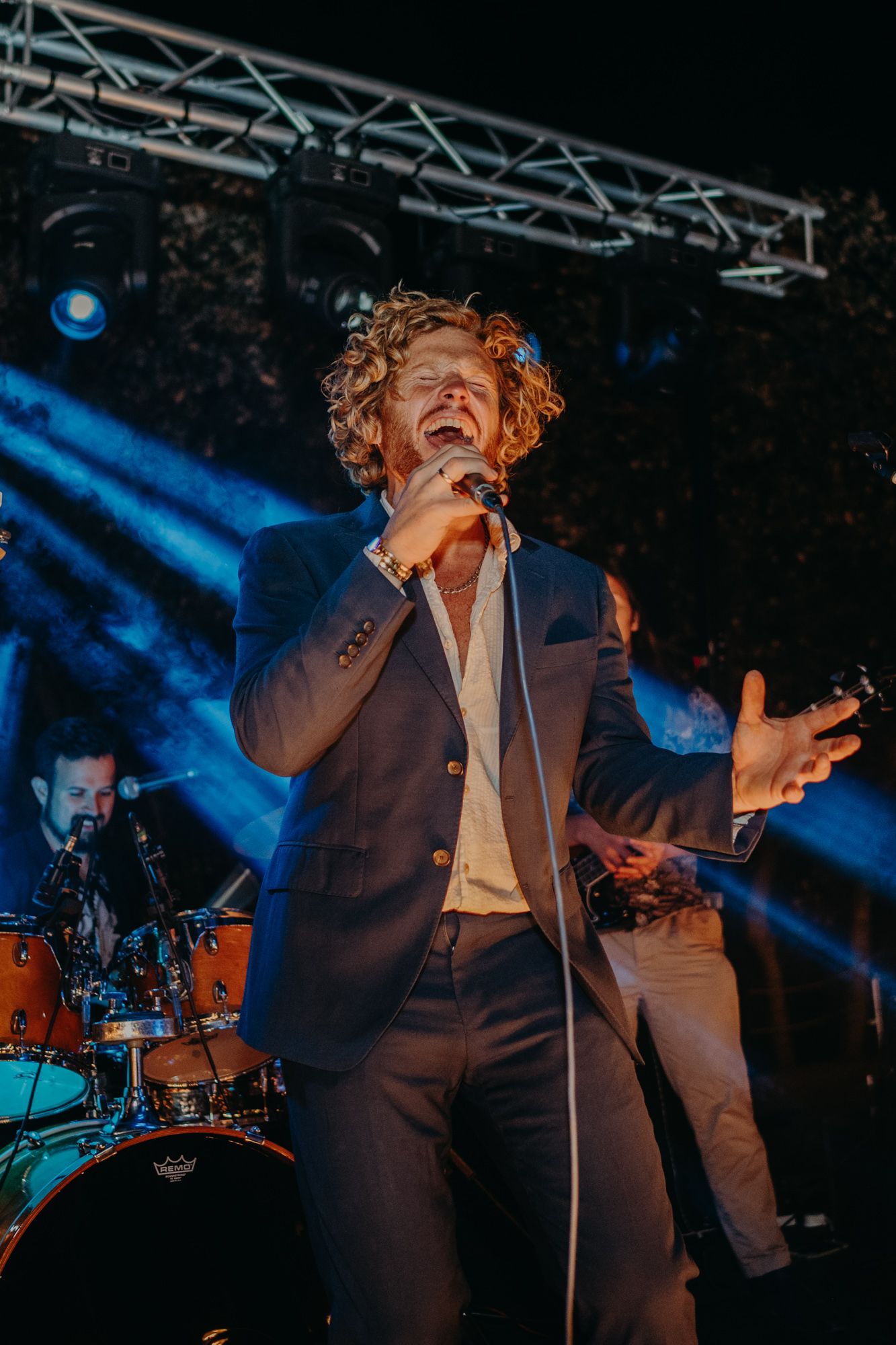 Singer performs passionately on stage with dramatic blue lighting and band in background.