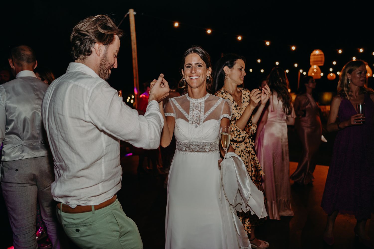 A couple dancing at their wedding reception under string lights during evening celebrations.