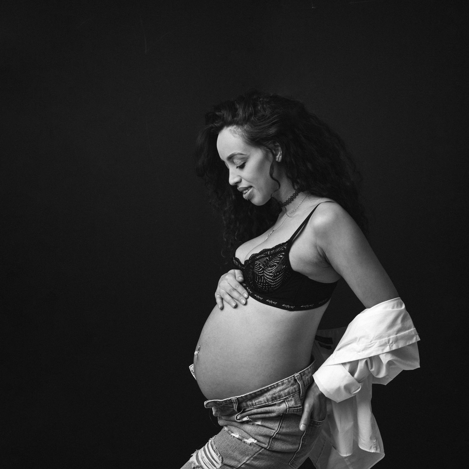 Beautiful black and white image of a maternity session with a woman in a black bra looking lovingly down at her baby to be.