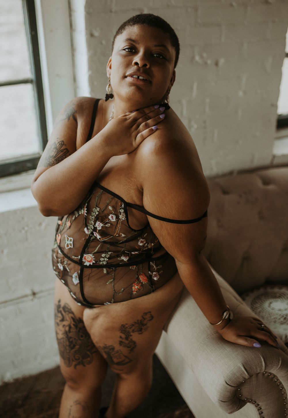 A boudoir photo shoot in a rustic room with soft lighting shows intimate lounging and tattoo art details.