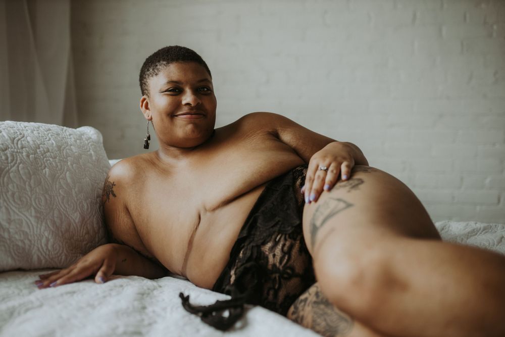 A person wearing black lingerie reclines on the bed during a cozy and intimate boudoir photoshoot.
