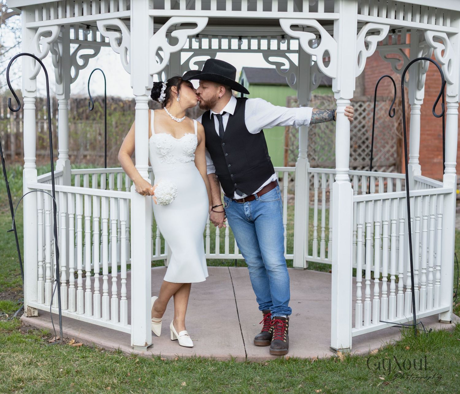 A romantic moment captured under a white wooden gazebo in a garden setting.