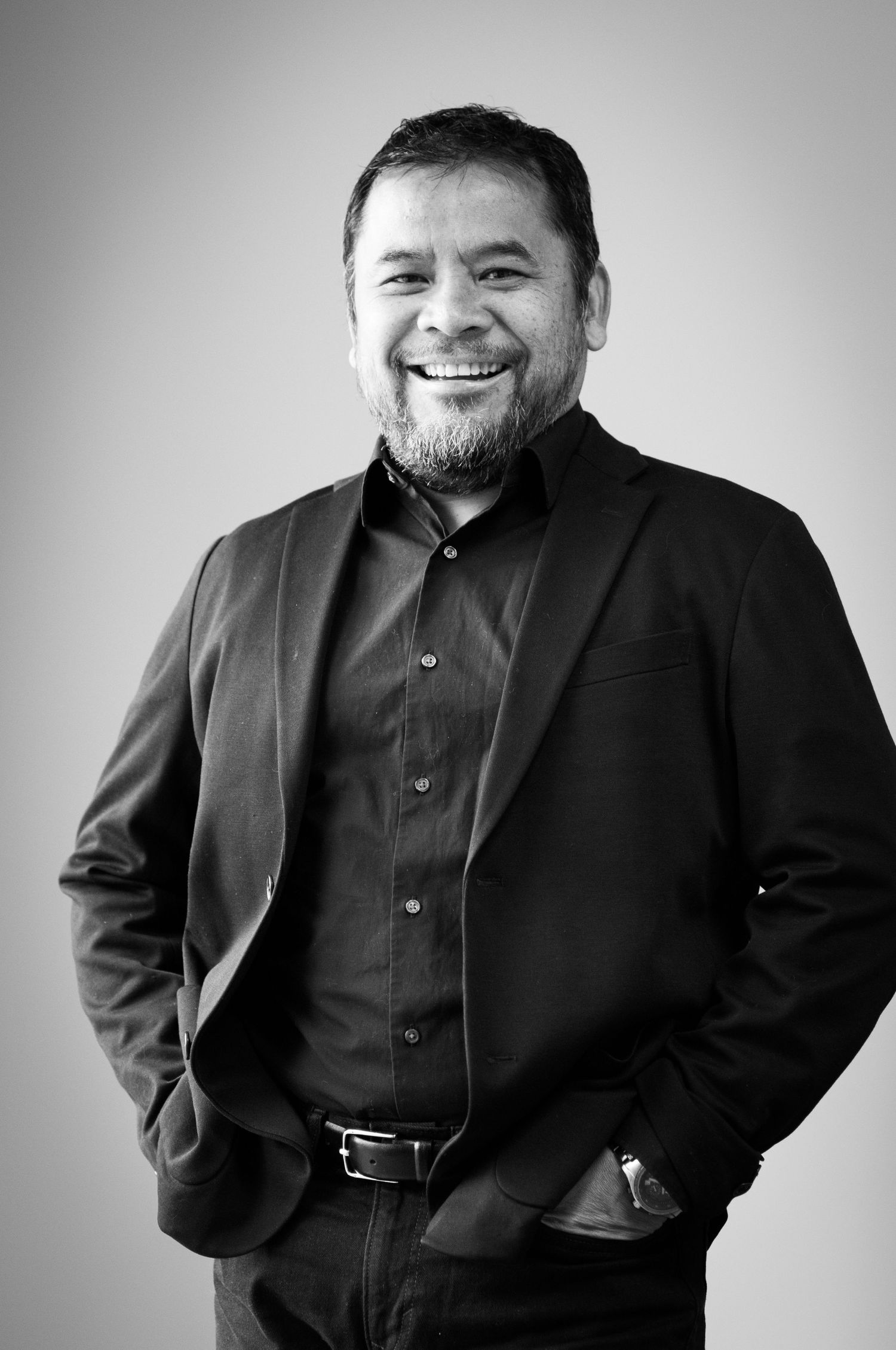 Professional black and white portrait of a smiling bearded man wearing a dark suit jacket and button-down shirt.