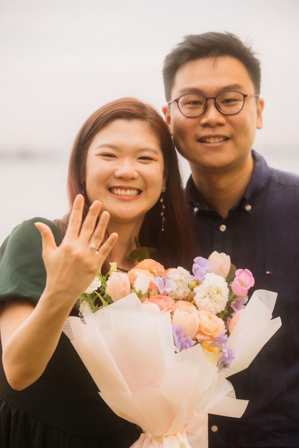 A couple celebrates their engagement moment with a beautiful bouquet of pink and purple flowers.