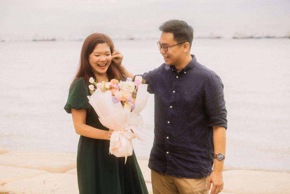 A couple shares a joyful moment at the beach while holding a pink and white flower bouquet.