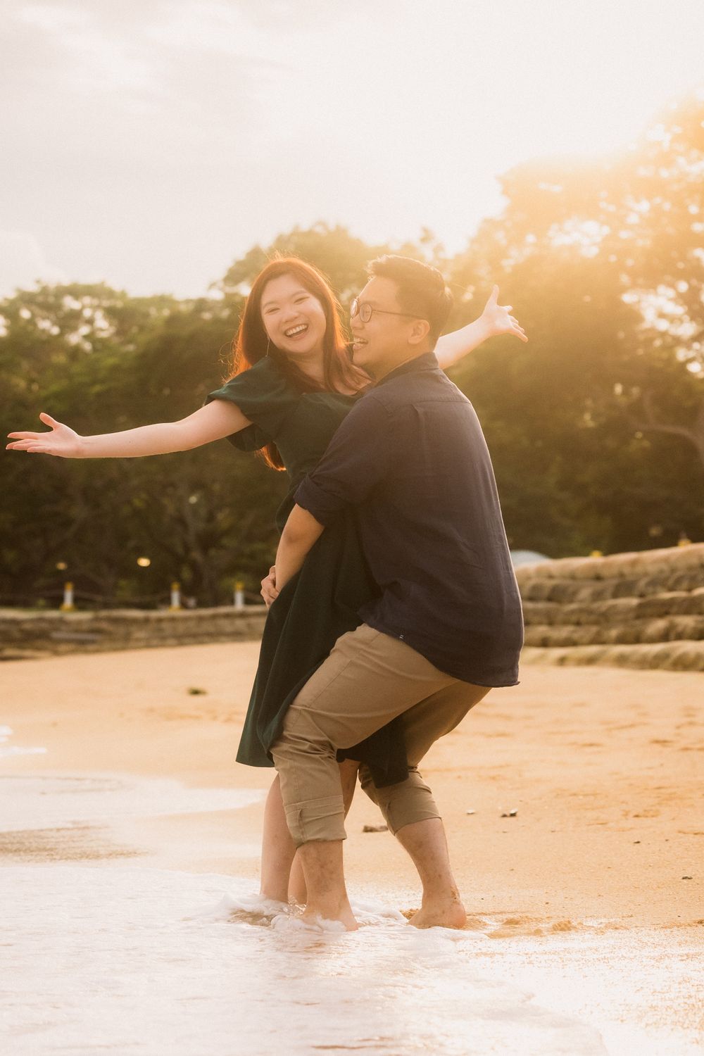 Couple enjoying a playful moment on the beach at sunset, splashing in the waves and laughing together.