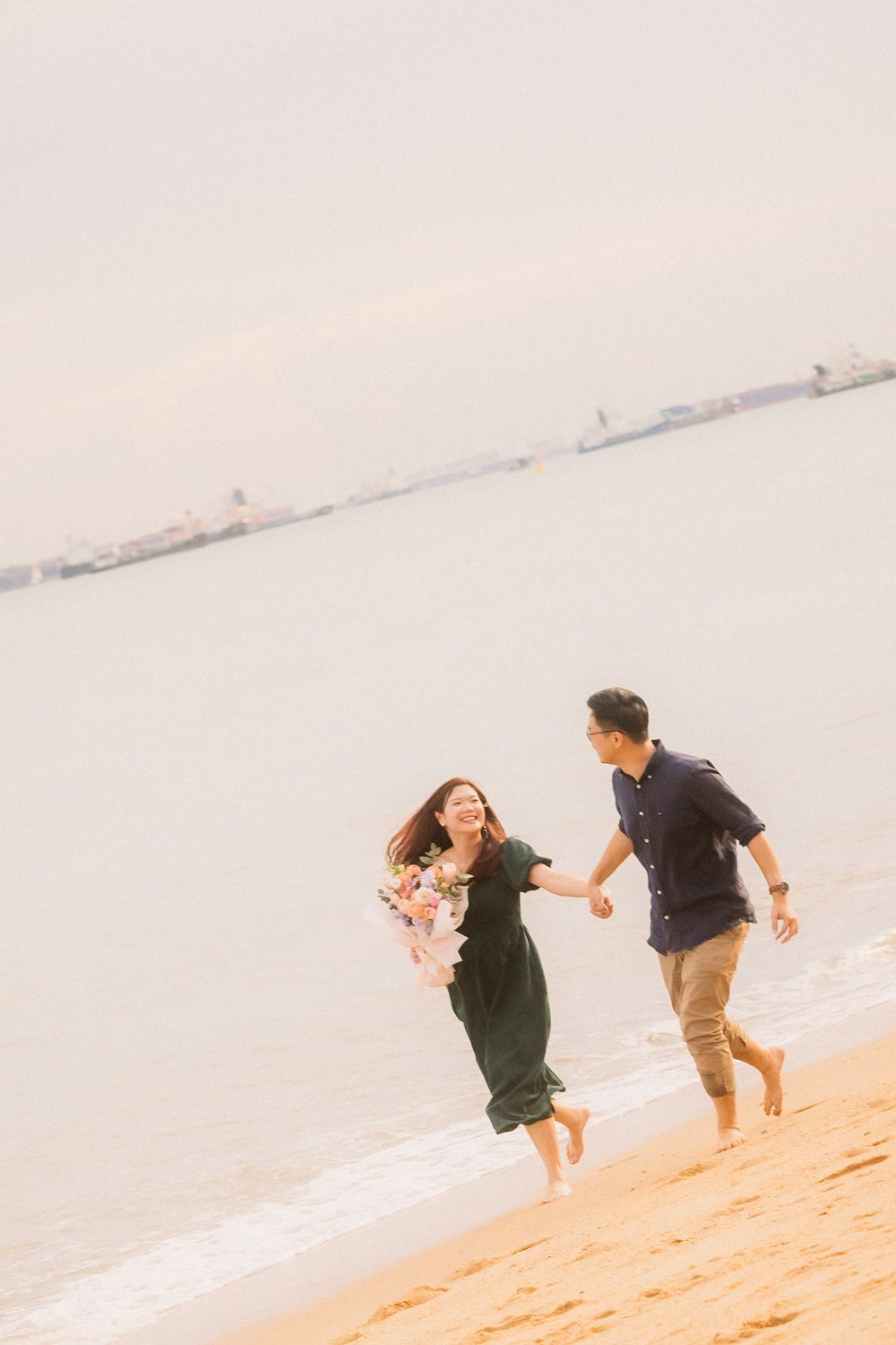 Romantic couple joyfully running together barefoot on a sandy beach at sunset.