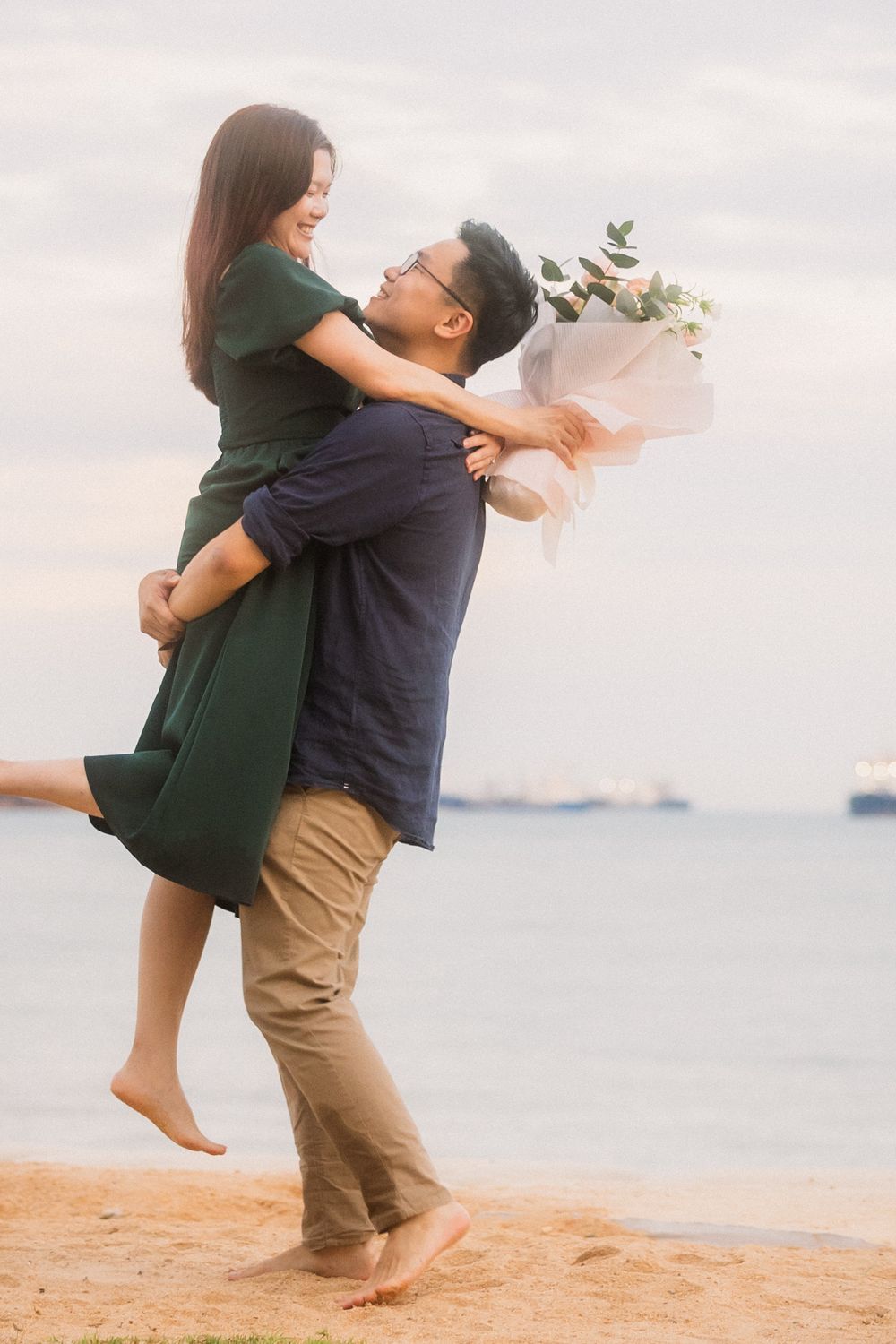 Couple sharing an intimate moment on the beach with a bouquet as the sun sets over the water.