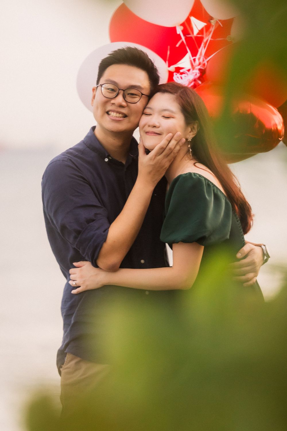 A romantic couple embraces outdoors with blurred red and green bokeh elements in the background.