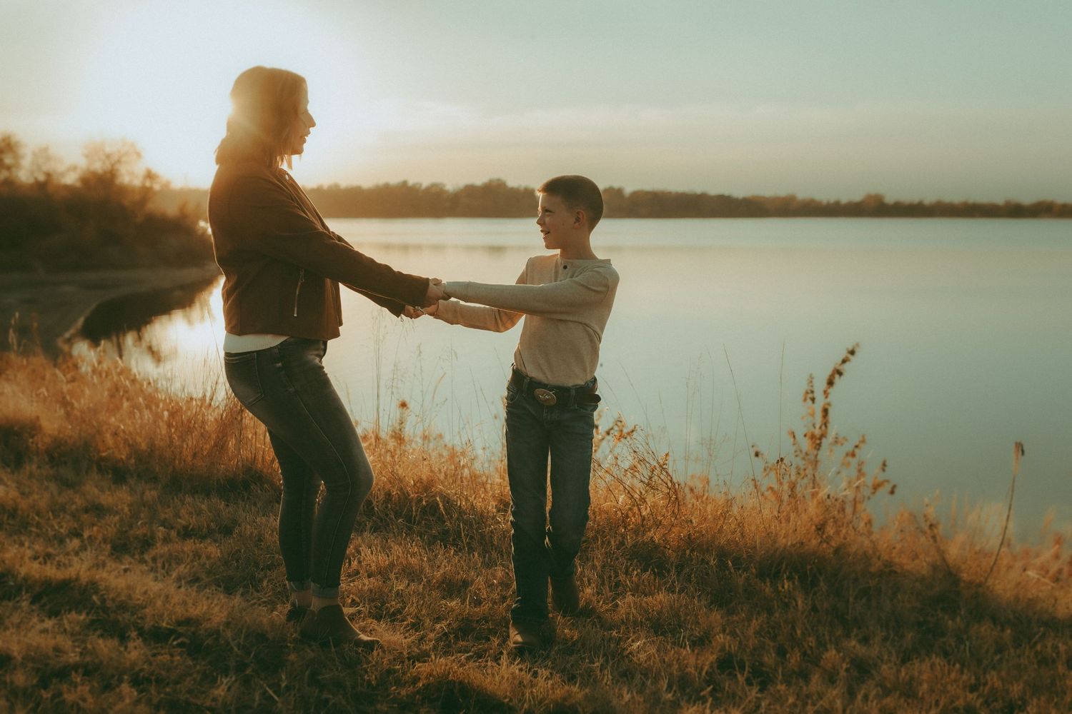 Mother and son holding hands by the lake at sunset – playful, storytelling family photography in Kansas