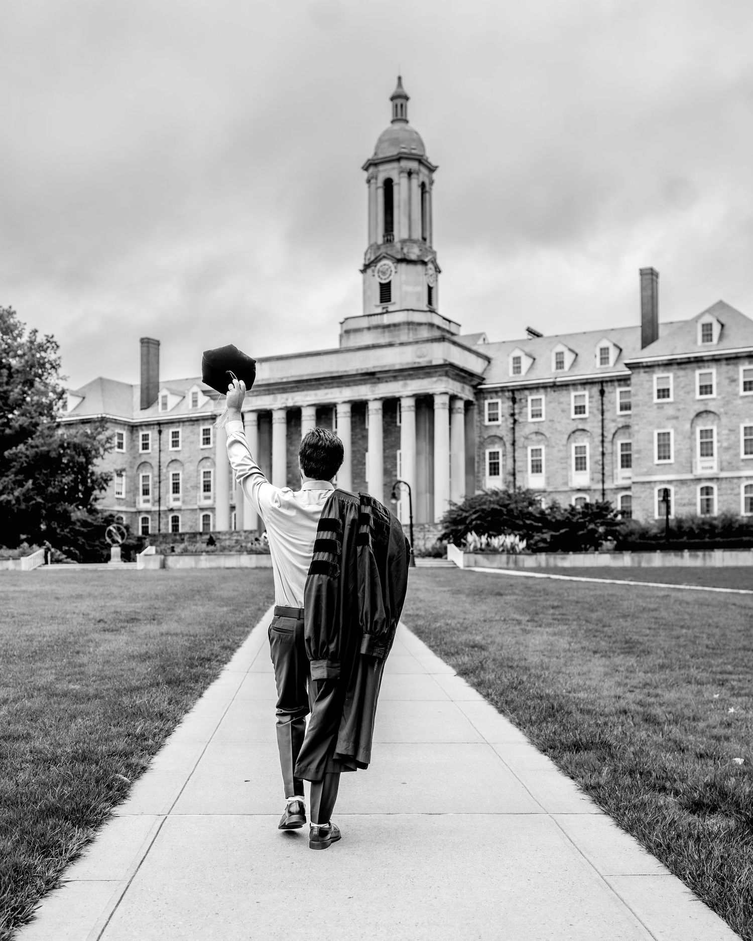 A black and white view of students walking on a pathway towards an old collegiate building with neoclassical architecture.