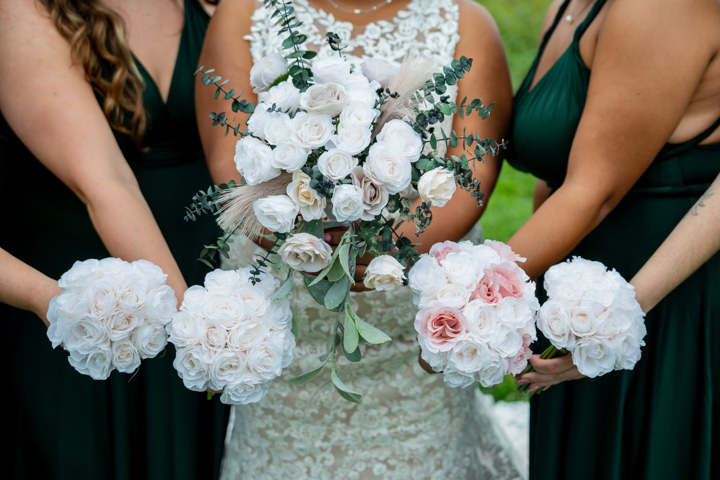Bridesmaids in emerald green dresses hold beautiful white and blush pink peony bouquets at an outdoor wedding.