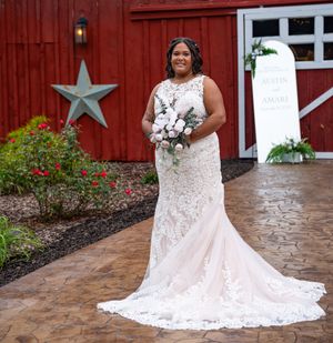 A bride in a white lace wedding dress poses in front of a red barn with decorative white stars.