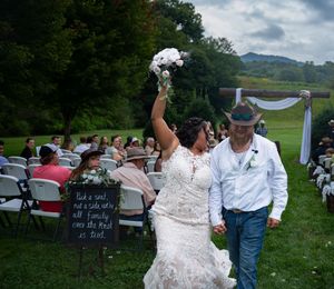 A festive outdoor celebration with guests seated on lawn chairs in a scenic countryside setting.