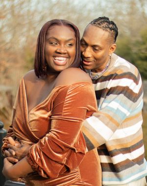 A joyful couple embraces outdoors, with one wearing a velvet rust-colored dress and the other in a striped sweater.