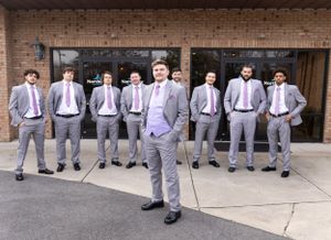A wedding party of groomsmen wearing matching gray suits and pink ties pose together outside a brick building.