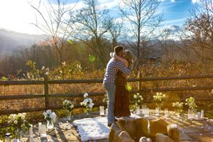 Scenic mountain wedding ceremony setup with white chairs and floral arrangements against a backdrop of autumn trees.