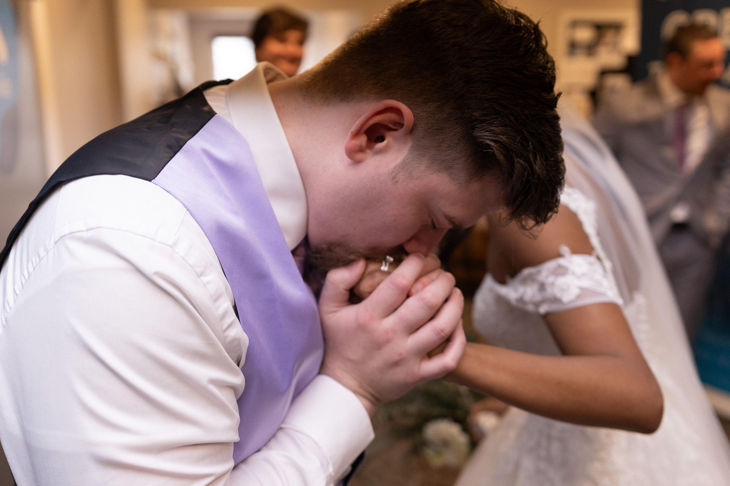An emotional groom in white vest covering his face with hands during the wedding ceremony.