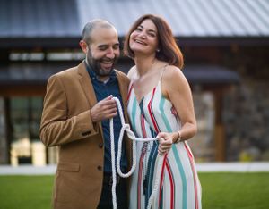 A couple shares a joyful moment outdoors on a summer day, with one wearing a striped dress and another in a brown blazer.