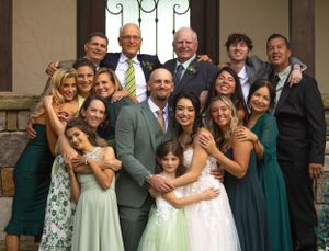 Wedding party in mixed formal attire including emerald green dresses poses together on stone steps outdoors.