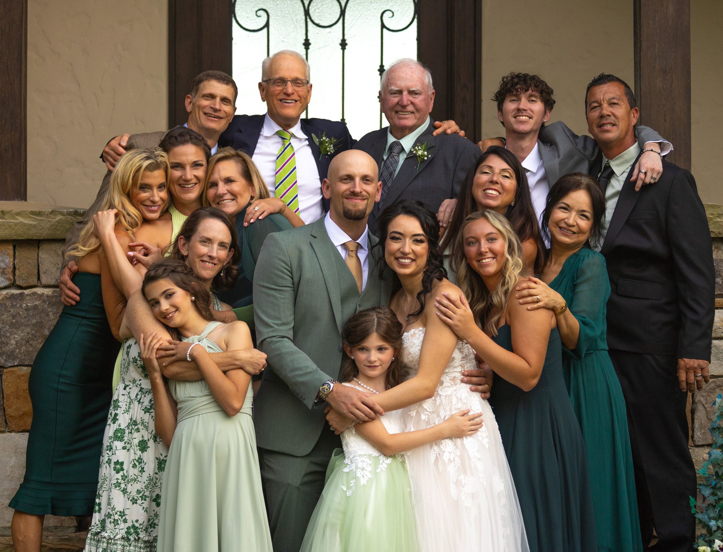 Wedding party in mixed formal attire including emerald green dresses poses together on stone steps outdoors.