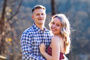 A couple embraces outdoors during an autumn engagement photo session with golden sunlight filtering through trees.