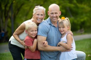 Happy family of four smiling together outdoors on a sunny day in a green park setting.