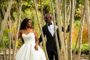 A bride and groom pose between white birch trees on their wedding day in an autumn outdoor setting.