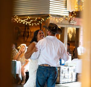 A couple dancing together in a warmly lit room with string lights and decorative elements in the background.