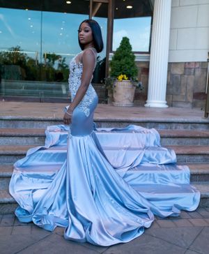 Someone poses in a stunning light blue mermaid-style gown with lace details and dramatic train on stone steps.
