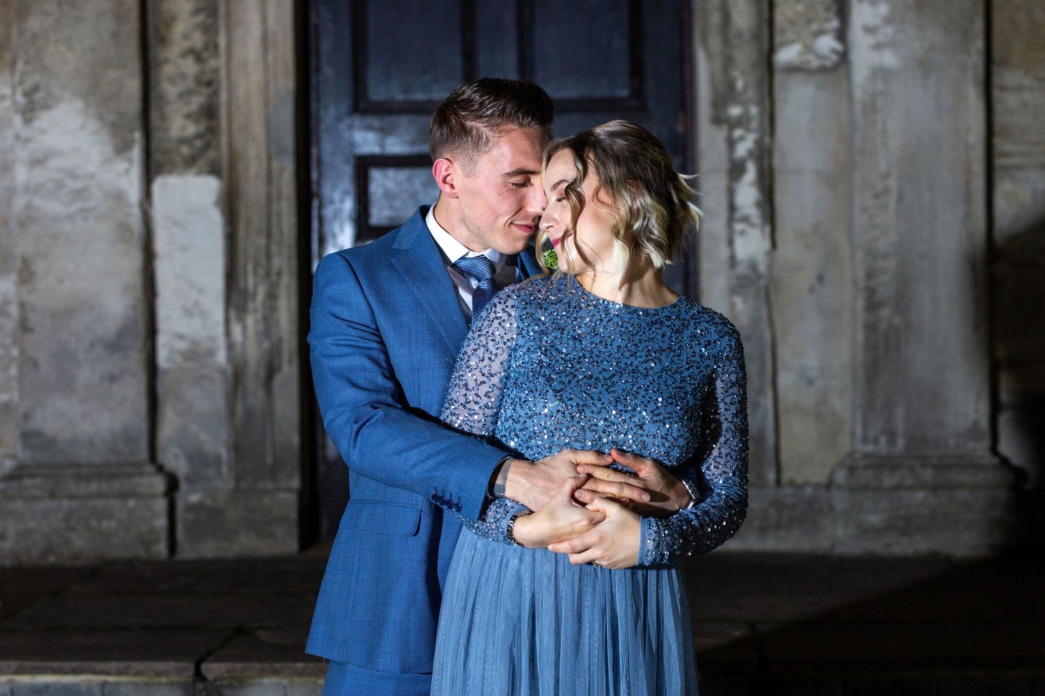 Couple in formal attire sharing intimate moments in front of an industrial backdrop.