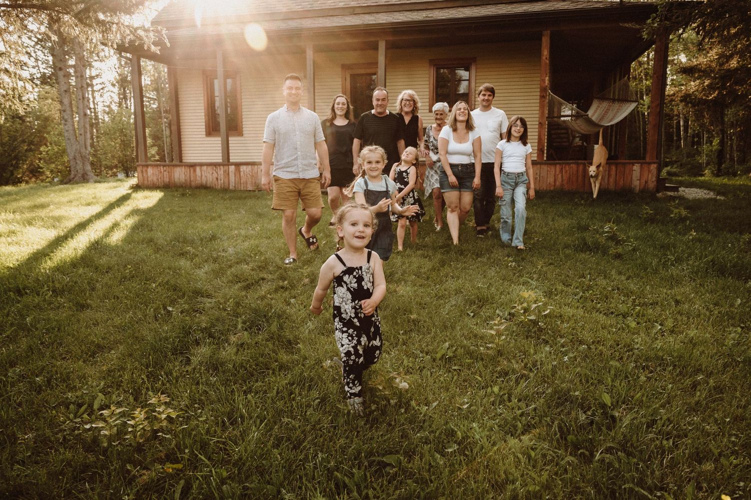 Family gathering outside a rustic cabin with sunlight filtering through the trees.