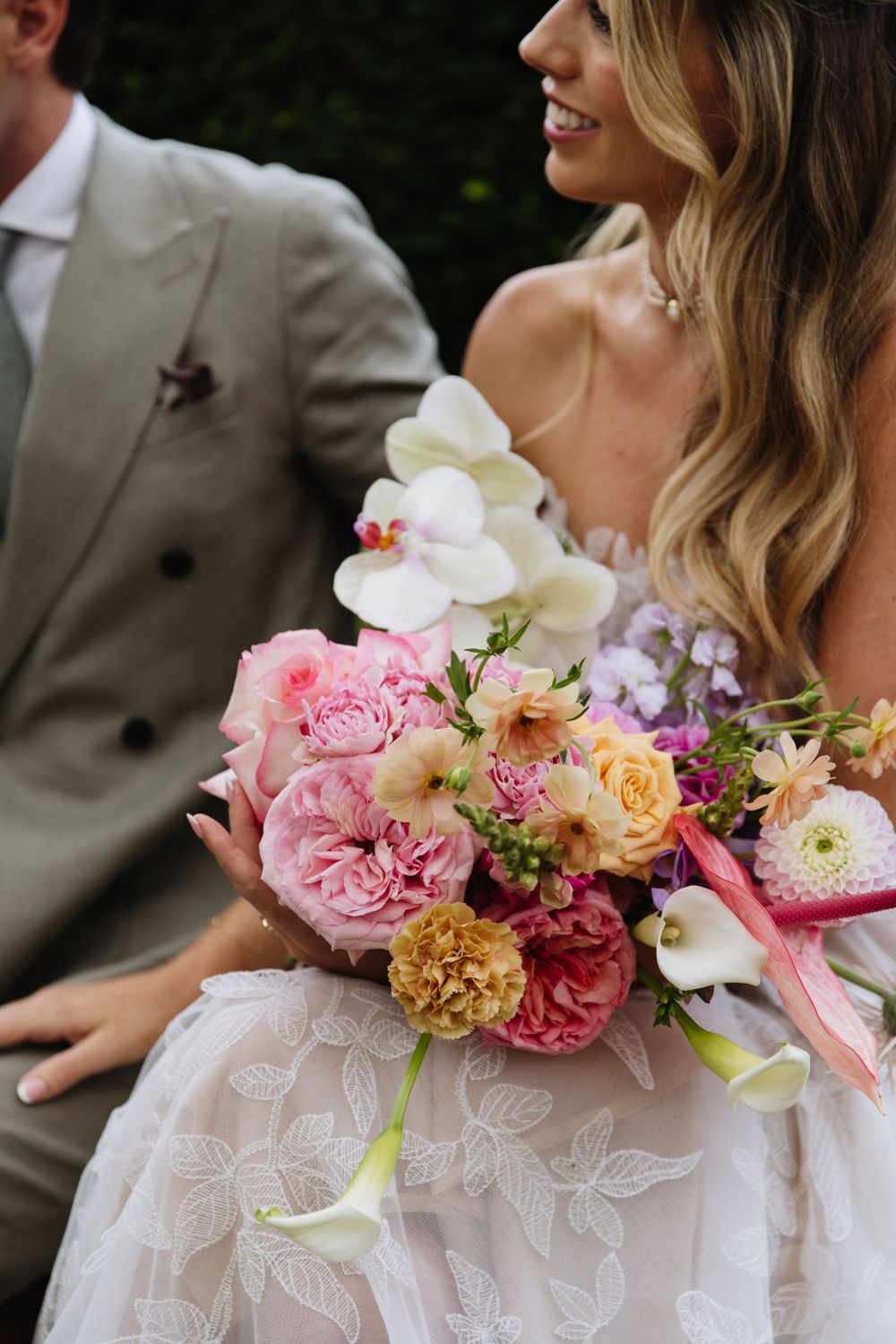 Beautiful bridal bouquet with pink garden roses, orchids and dahlias against a white lace wedding dress.