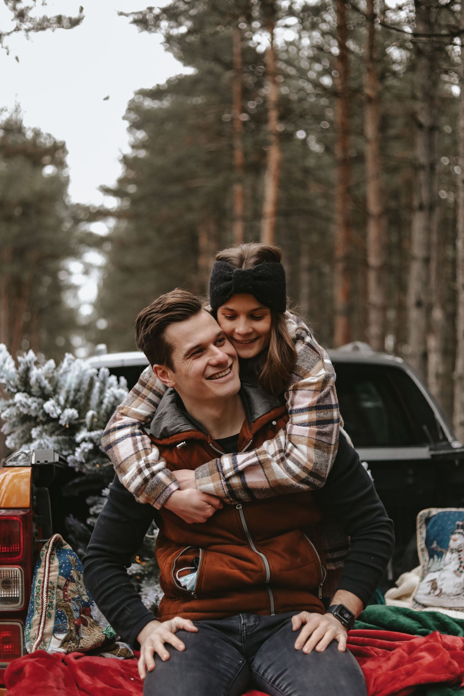 A couple shares a playful moment while sitting in the back of a pickup truck surrounded by pine trees.