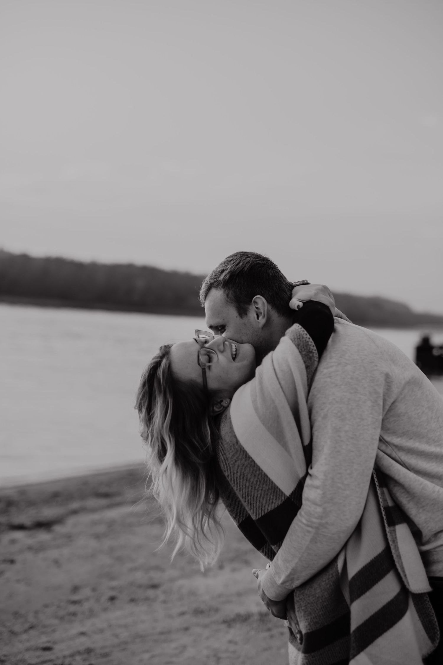 A romantic black and white photo of a couple embracing on a beach shore.