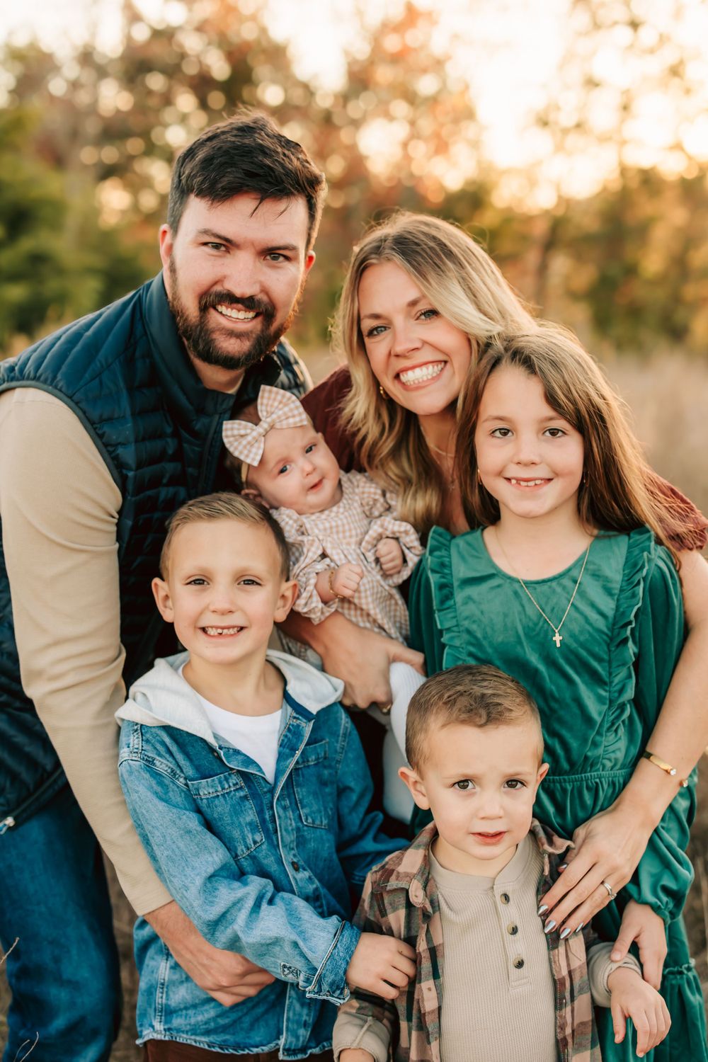 A cheerful family of six poses together outdoors at sunset with golden bokeh lighting in the background.